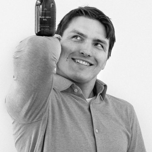 A smiling man holds a brown glass bottle containing a Marinus skin care product over his shoulder. Simple presentation.