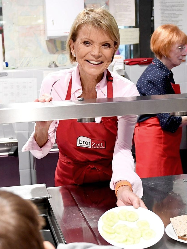 Uschi Glas smilingly serves food to children