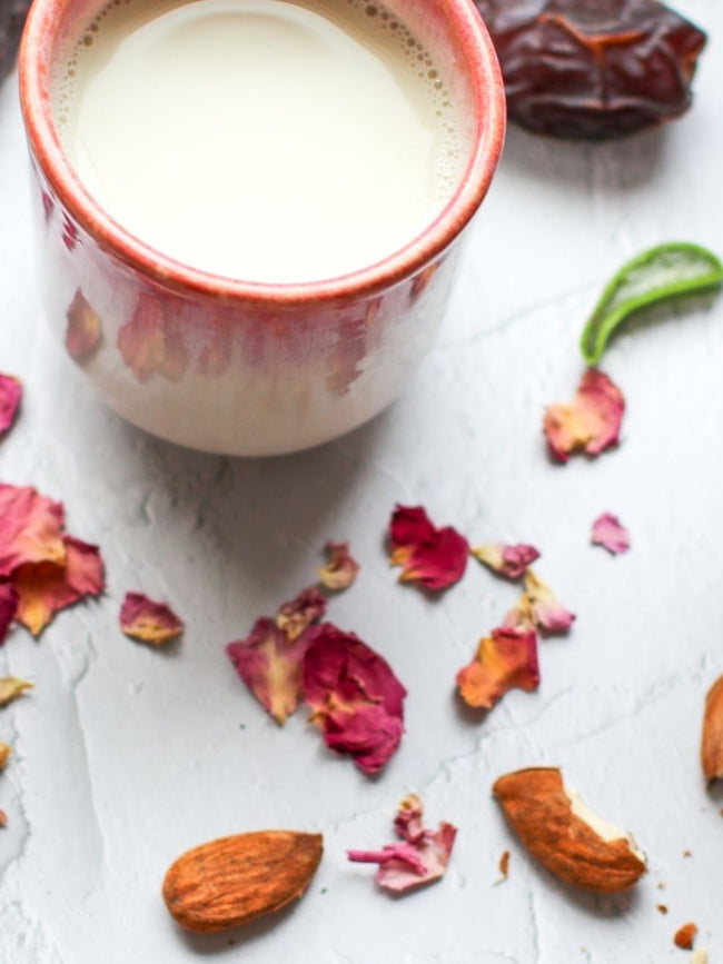 You can see the ingredients for a smoothie. Frozen raspberries in a bowl, almonds, aloe vera strips and dried rose petals.