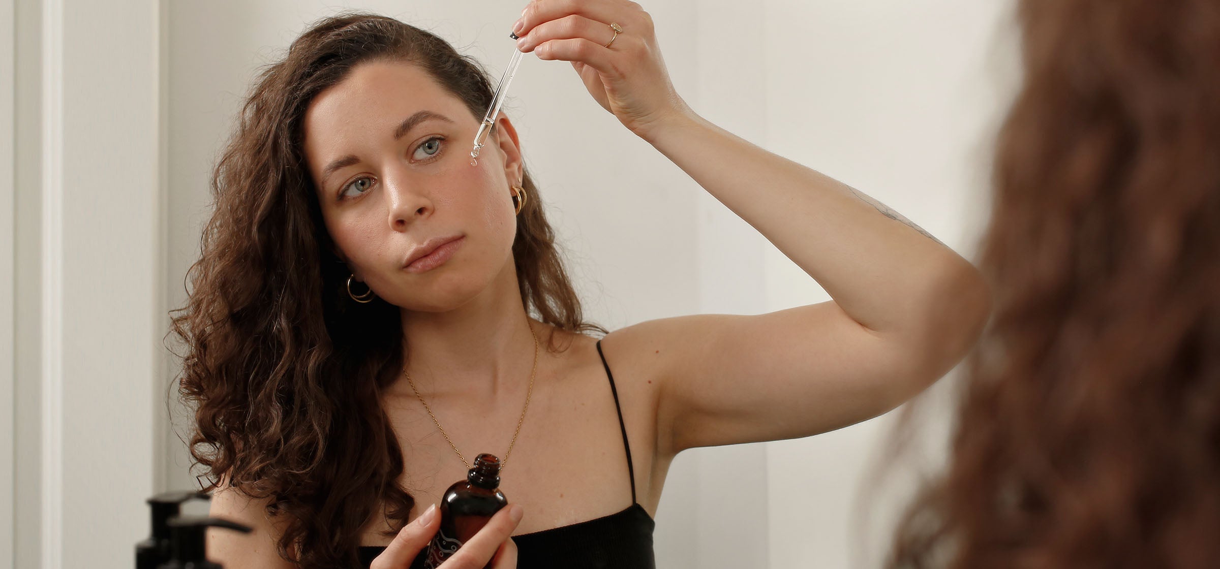 Woman with fair skin dripping a facial oil onto her cheek with a pipette