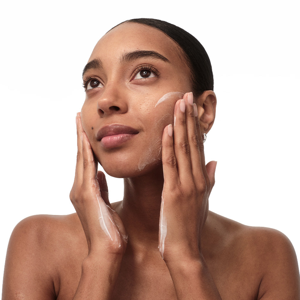 A woman with a fresh complexion applies a light layer of " cream " to her face. Her skin looks hydrated.