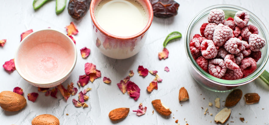 You can see the ingredients for a smoothie. Frozen raspberries in a bowl, almonds, aloe vera strips and dried rose petals.