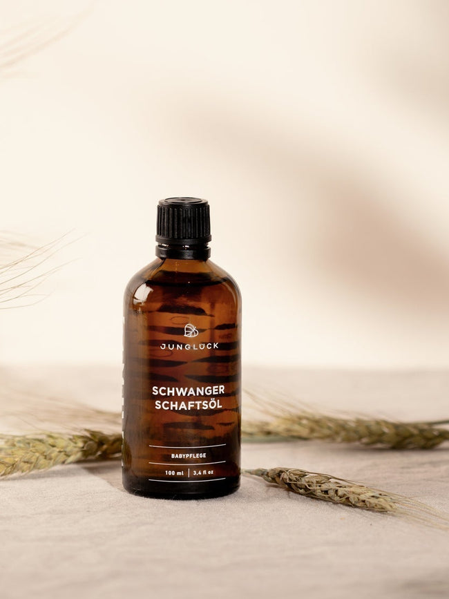The bottle of Pregnancy Oil stands against a beige background decorated with wheat stalks.