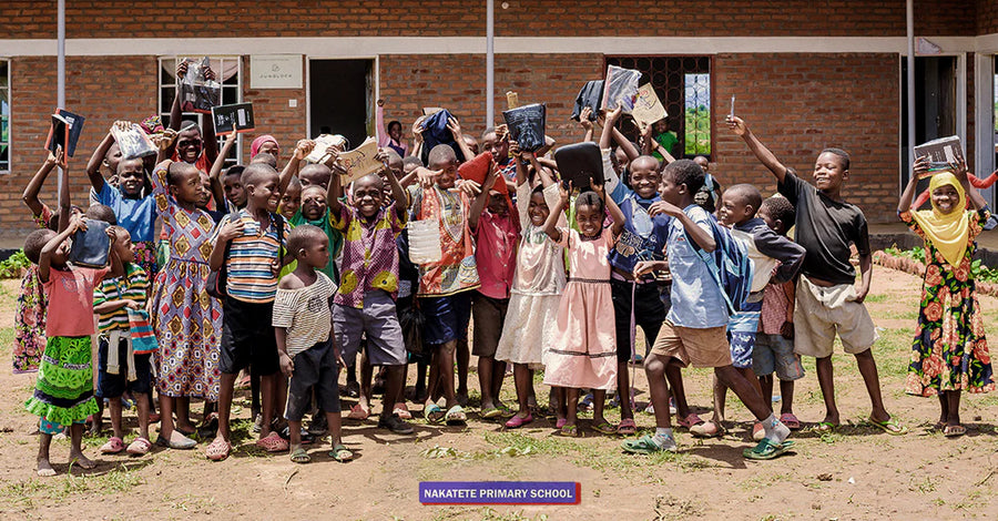 A group of children in front of Nakatete Primary School in Malawi, holding up books and school supplies.