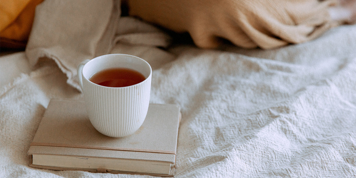 Teacup and book on a white-covered bed