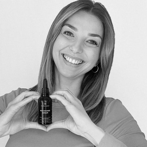 A woman with long hair, wearing a sweater, is holding a heart-shaped amber glass bottle in front of her chest.