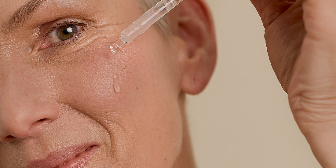 A woman applies drops of Retinal serum to her face with a pipette, in what appears to be a skincare ritual.