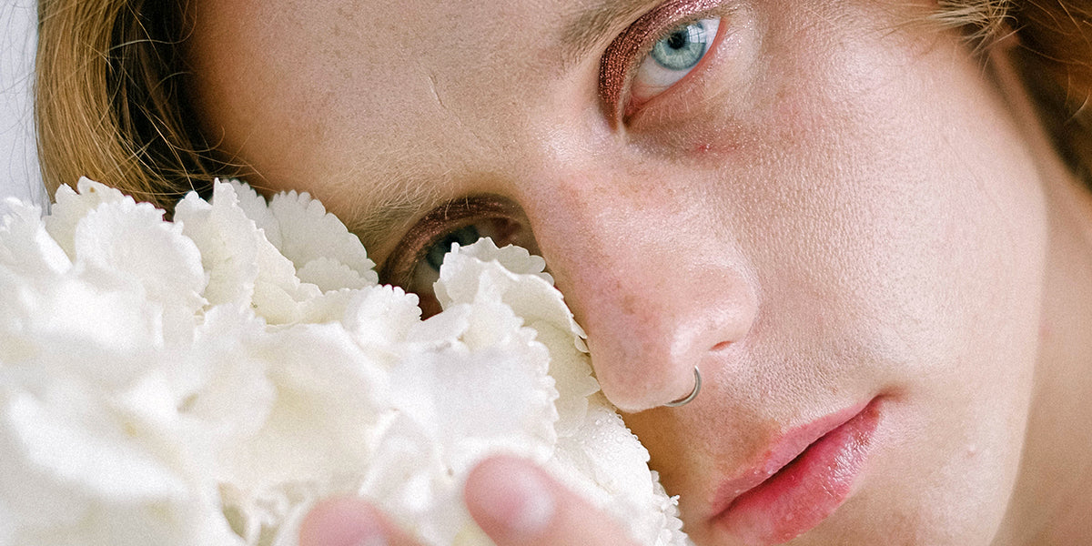 The face of a non-binary person, with a delicate blossom on the cheek