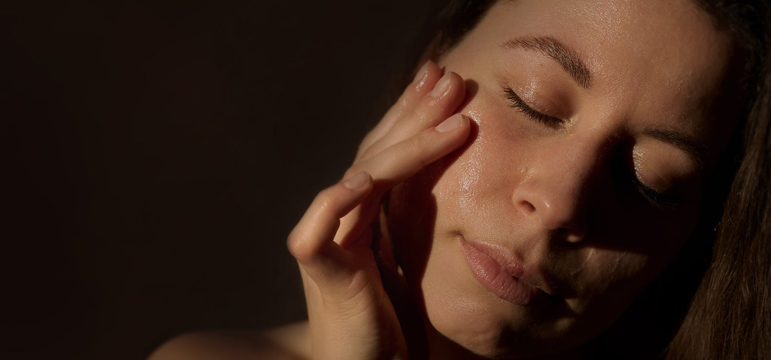 A close-up of a woman gently touching her cheek. Soft lighting highlights her facial features.