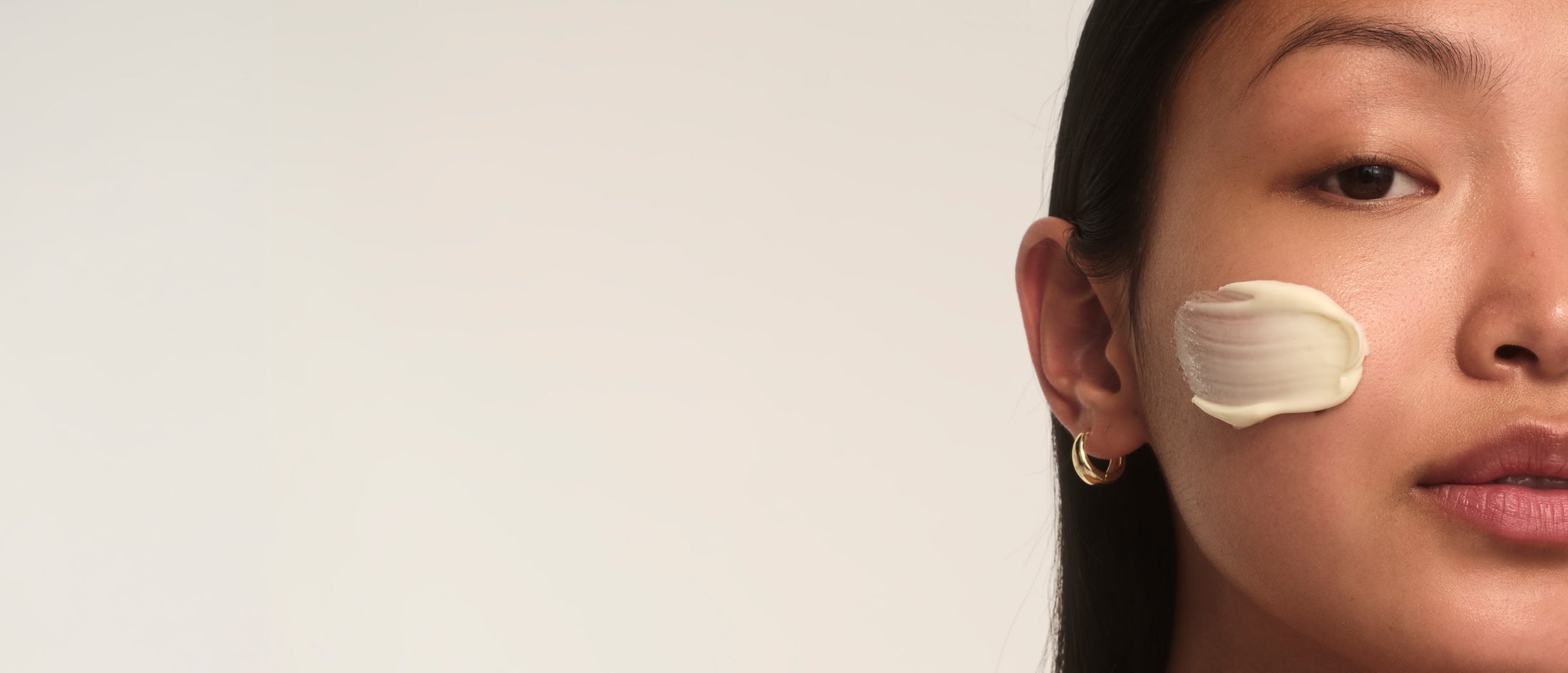 A woman with a creamy product on her cheek, against a light background.