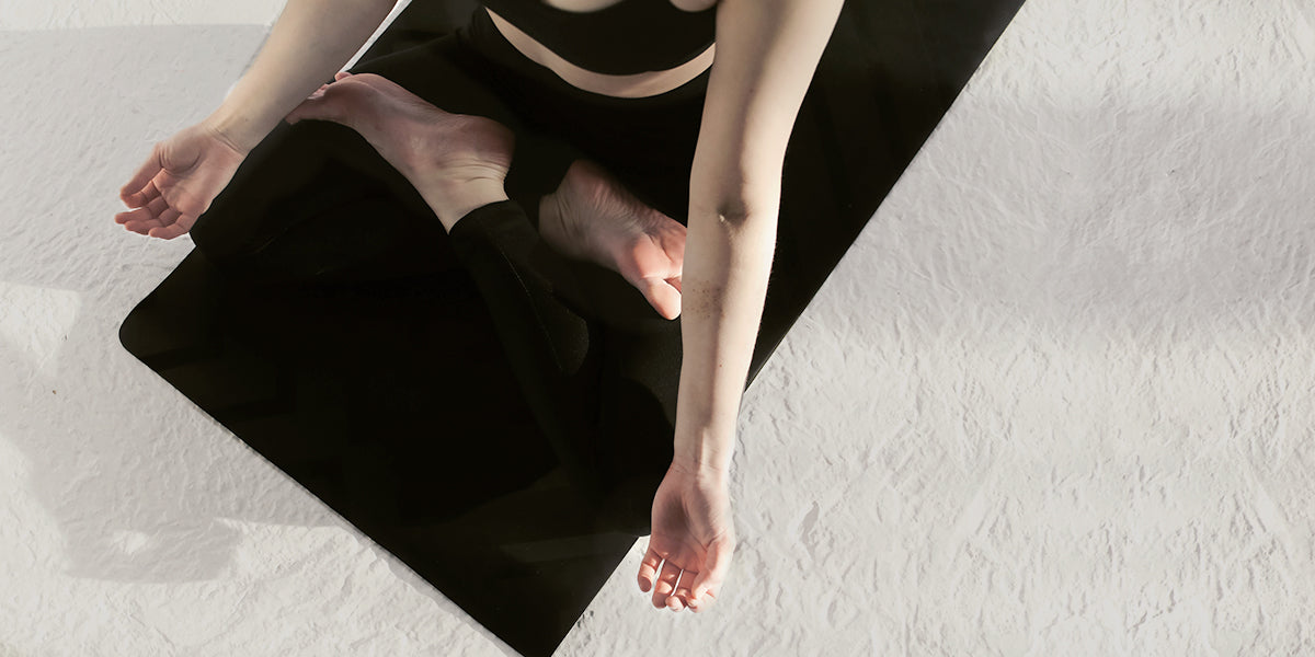 A bird's eye view of a woman sitting cross-legged on her yoga mat.