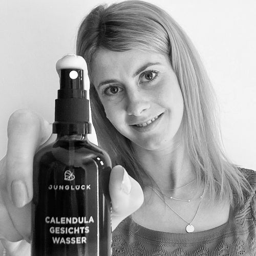 A person holds a brown glass bottle of JUNGLÜCK's Calendula toner up to the camera. The label is clearly legible.