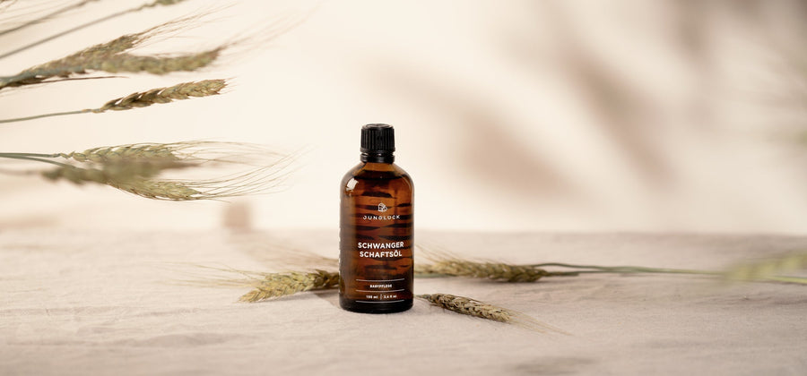 The bottle of Pregnancy Oil stands against a beige background decorated with wheat stalks.